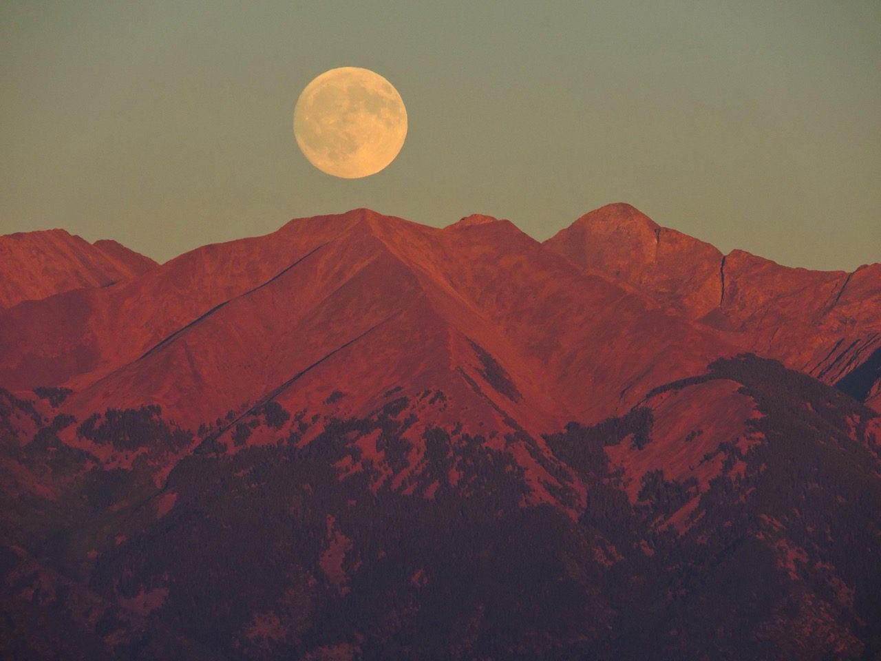 A large full moon rising orange above Blanca Peak, seen from Great Sand Dunes National Park and Preserve